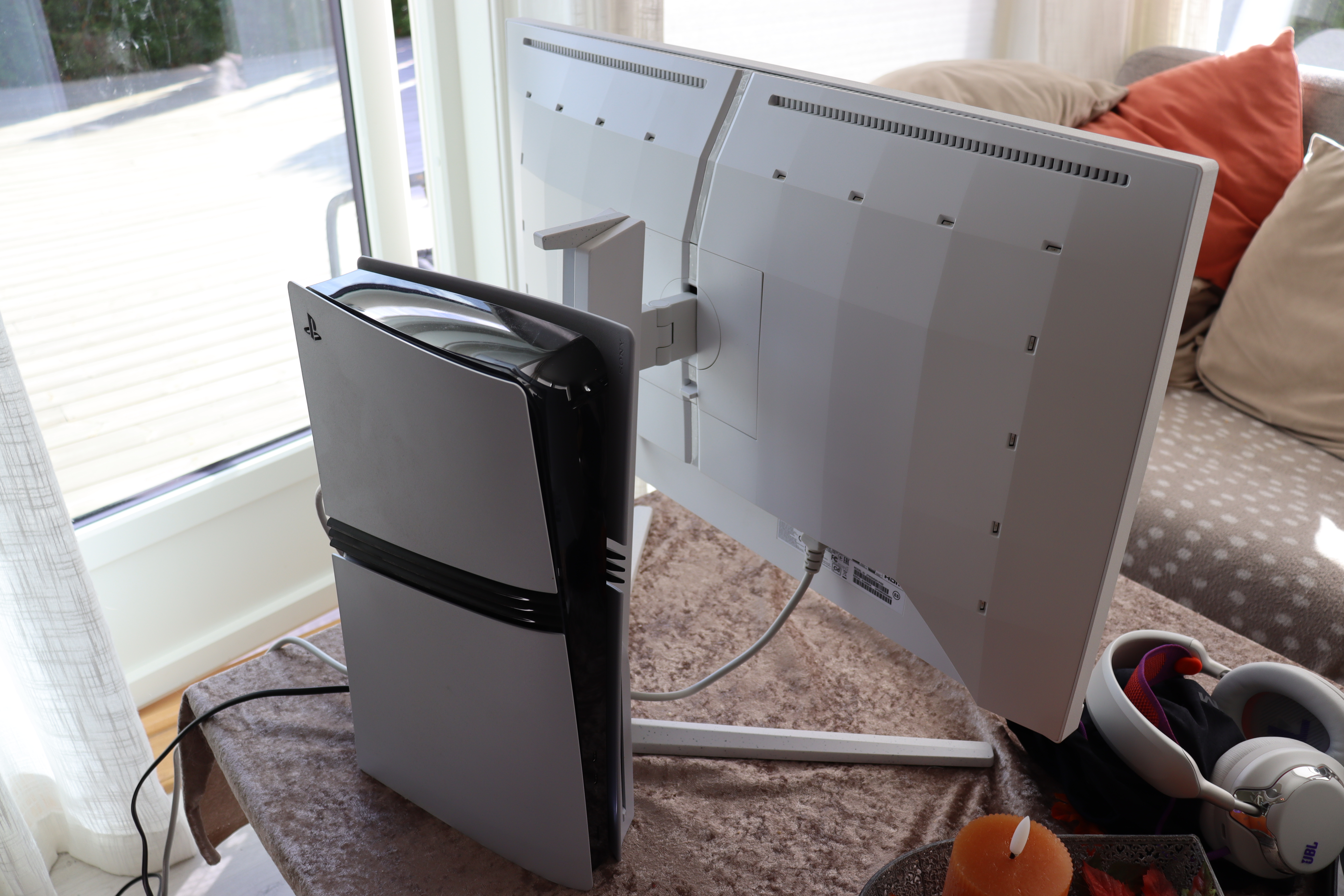 En moderne dataskjerm med en PlayStation-konsoll plassert ved siden av, på et bord ved et vindu.