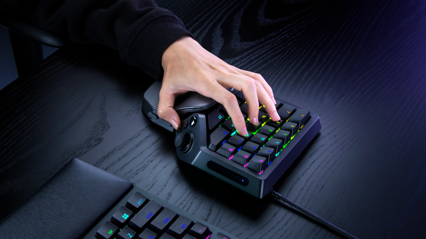 Hånd som bruker en ergonomisk spillkontroller med RGB-belysning på et skrivebord.